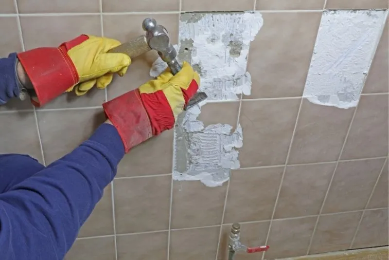 Gloved hands using a hammer to remove old tiles in Noosa